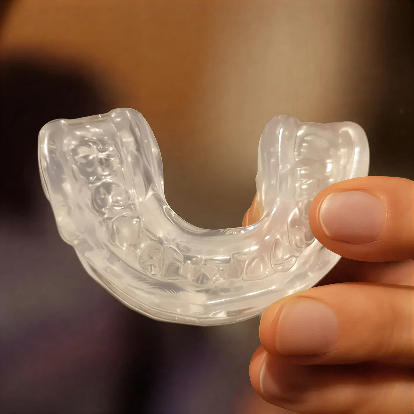 Clear mouthguard held in a hand against a blurred background
